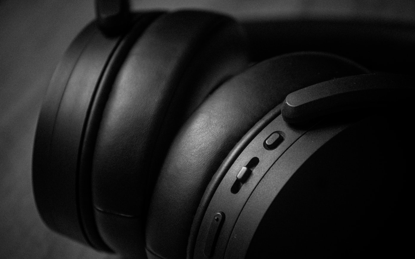 An over-ear headphone photographed close against a dark ground, earcup and hinge in shallow focus.