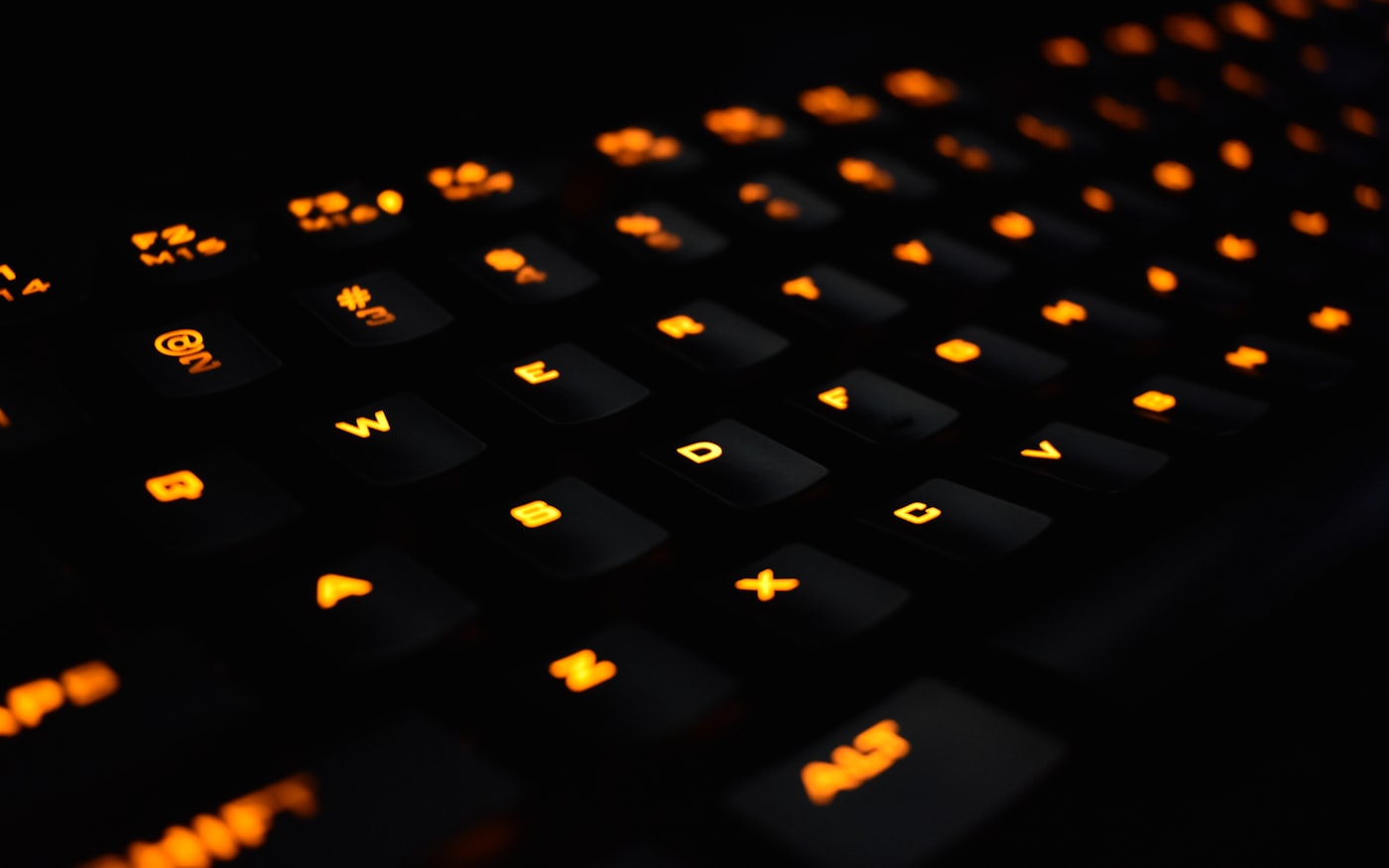 A backlit mechanical keyboard shot low, amber light spilling from under the keycaps.