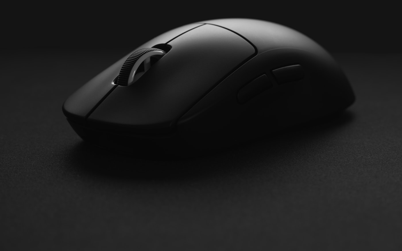 A black wireless mouse in profile on a dark desk, lit by a single source.
